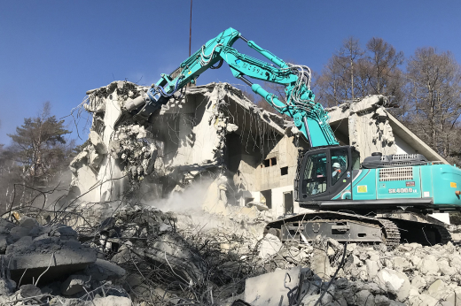 解体作業中の重機が建物を崩している現場の写真
